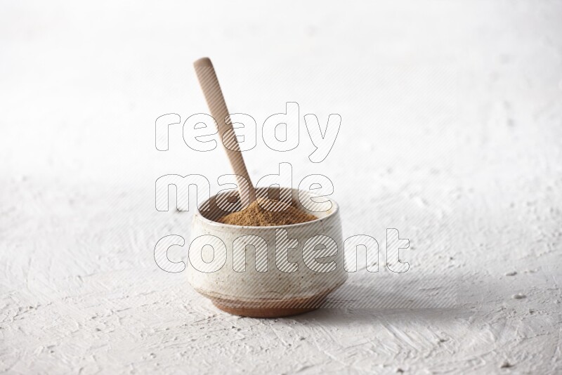 Ceramic beige bowl full of cinnamon powder with a wooden spoon on a textured white background