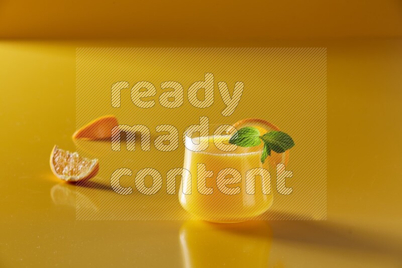 glass of orange juice with orange & mint  on yellow background
