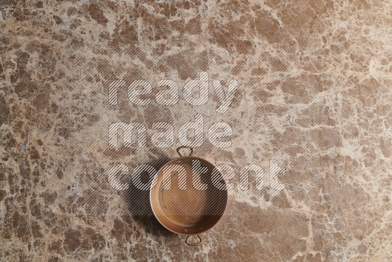 A small copper pan on beige marble background