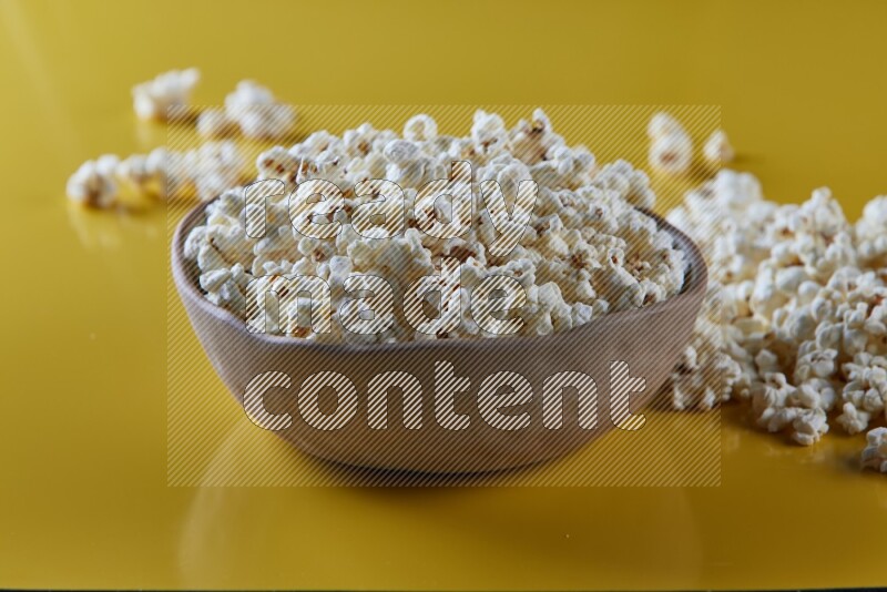A brown pottery bowl full of popcorn with popcorn beside it on a yellow background in different angles