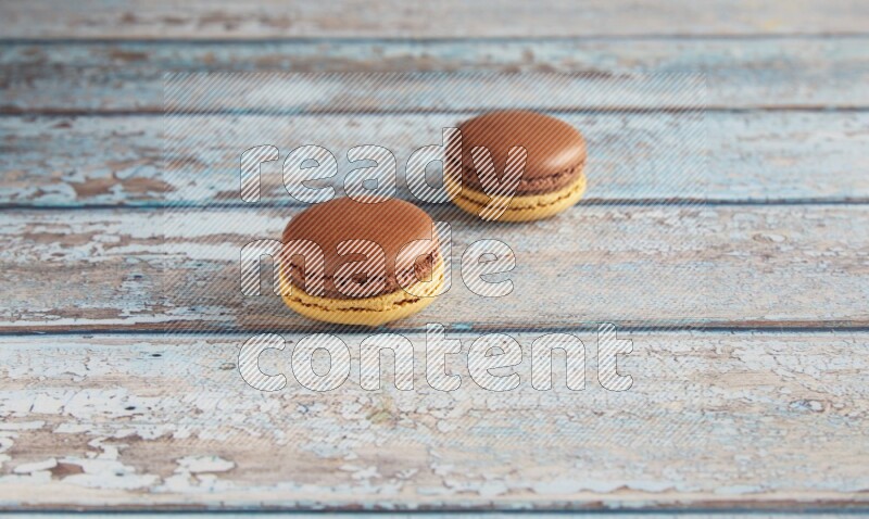 45º Shot of two Yellow and Brown Chai Latte macarons on light blue wooden background