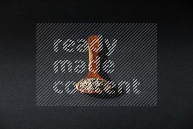 مغرفة خشبية ممتلئة بحبوب الكمون على خلفية سوداء