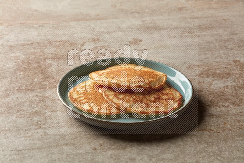 Three stacked plain pancakes in a blue plate on beige background
