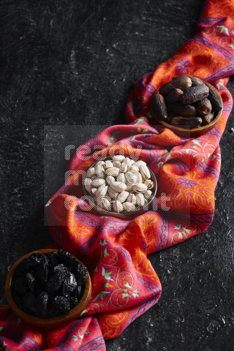 Dried fruits and nuts in wooden bowls in a dark setup