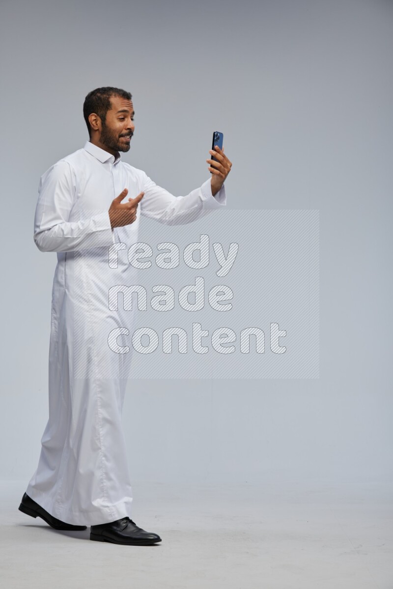 Saudi man wearing Thob standing taking selfie on Gray background