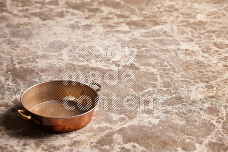 A small copper pan on beige marble background