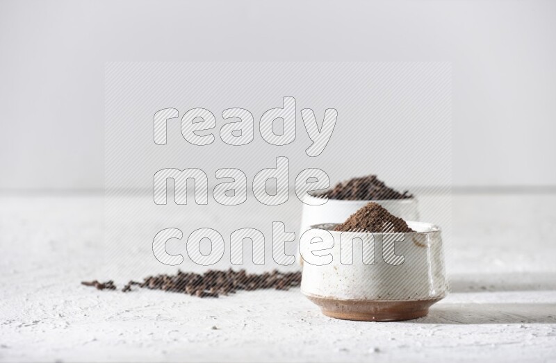 وعاءين من السيراميك بيج اللون، أحدهما مملوء بالقرنفل والآخر مملوء بالبودرة على أرضية بيضاء