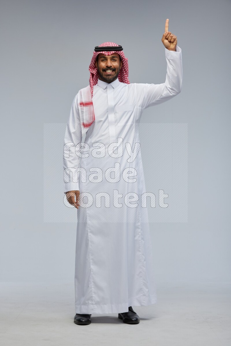Saudi man Wearing Thob and shomag standing interacting with the camera on Gray background
