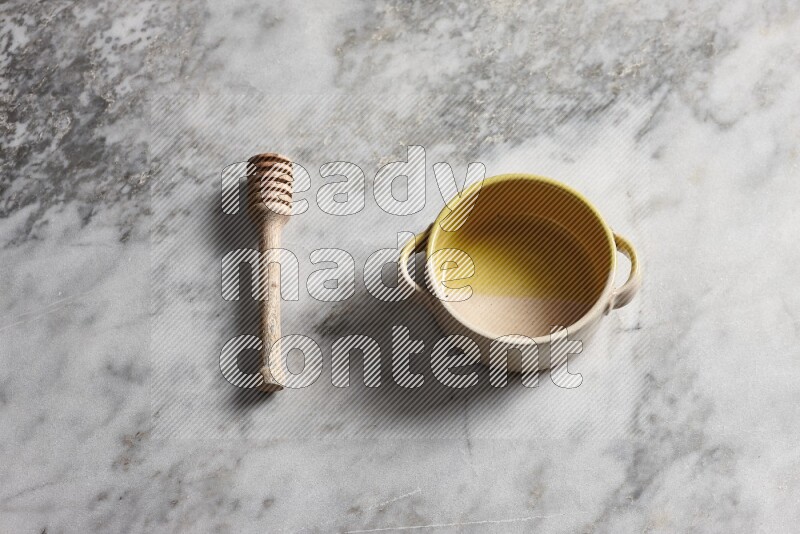 Multicolored pottery bowl with wooden honey dipper on the side on grey marble background