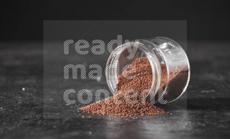 وعاء زجاجي مقلوب ممتلئ ببذور حب الرشاد وتناثرت البذور منه على أرضية سوداء