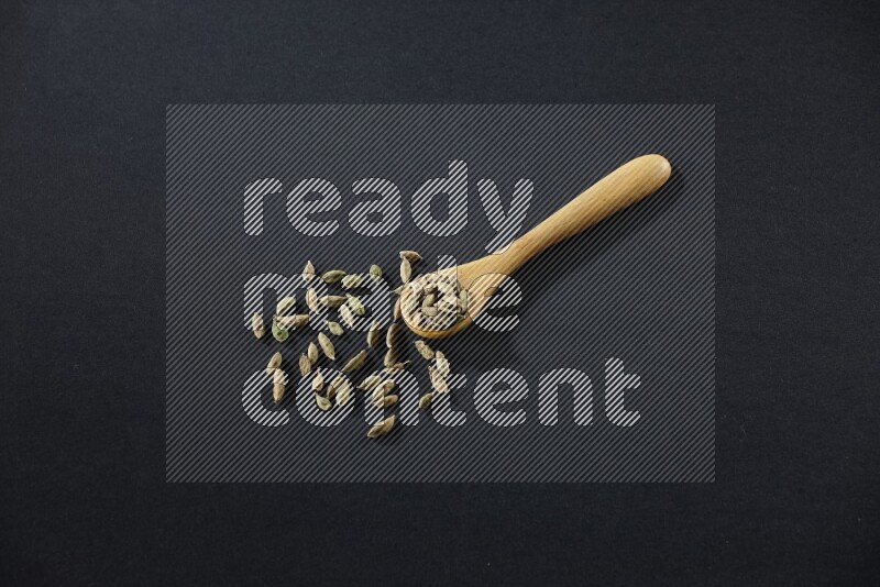 ملعقة خشبية ممتلئة بالهيل على خلفية سوداء