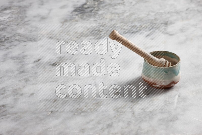 Multicolored pottery bowl with wooden honey dipper in it on grey marble background