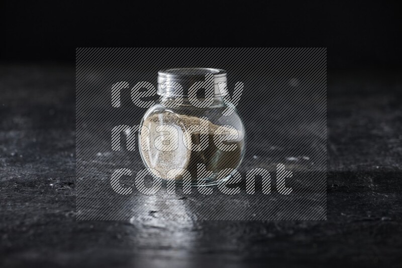 Herbal glass jar full of white pepper on textured black flooring