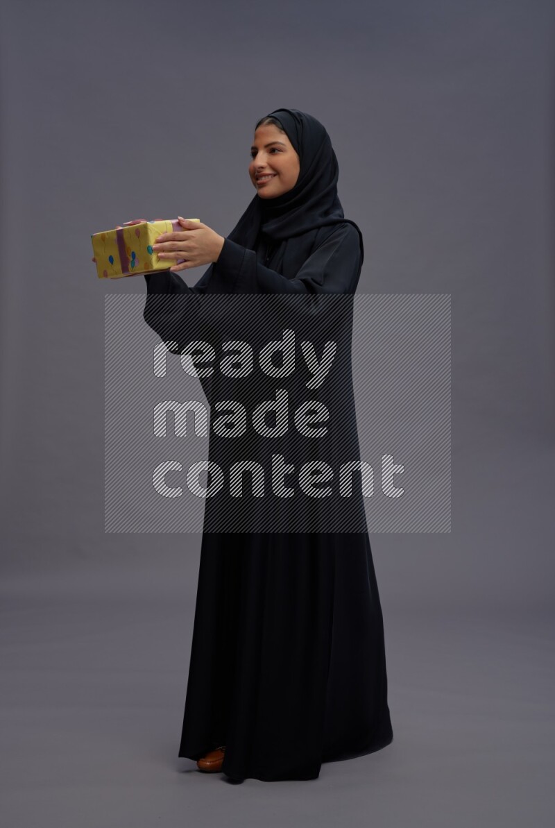 Saudi woman wearing Abaya standing holding gift box on gray background