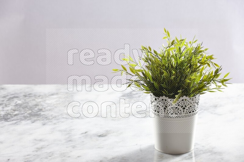 Green artificial plant in white decorative pot on grey marble background