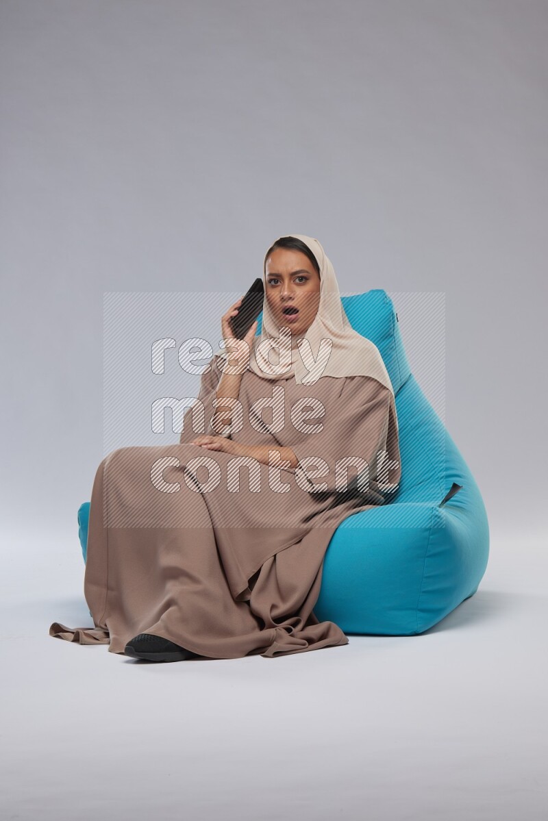 A Saudi woman sitting on a blue beanbag and working on laptop