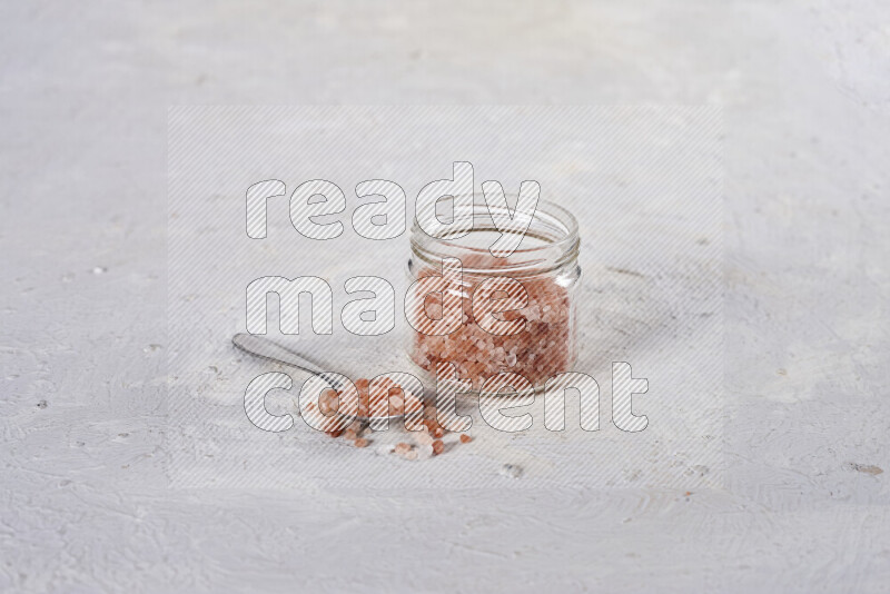 A glass jar full of coarse himalayan salt crystals on white background