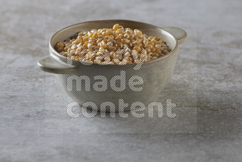 corn kernel in a off-white handheld ceramic bowl on a grey textured countertop