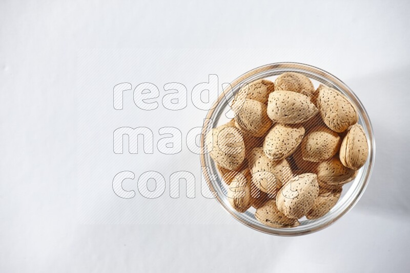 A glass bowl full of almonds on a white background in different angles
