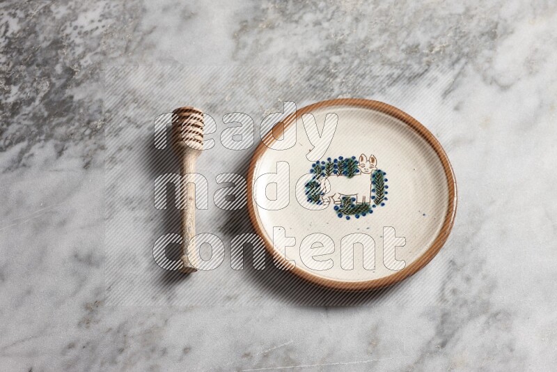 Decorative pottery plate with wooden honey dipper on the side on grey marble background