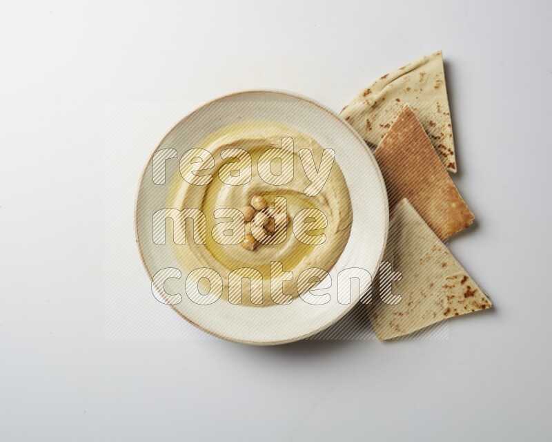 Hummus in a pottry plate garnished with roasted chickpeas on a white background