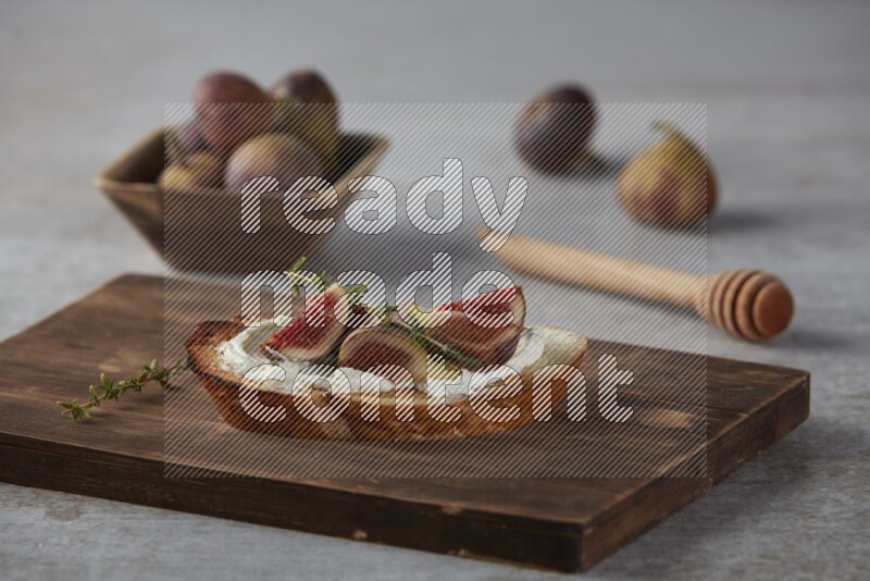 quarters of figs with cream cheese on toasted sourdough slice on a wooden board on textured grey background
