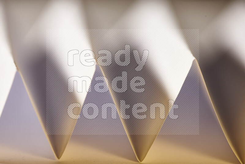 A close-up abstract image showing sharp geometric paper folds in white gradients and warm tones
