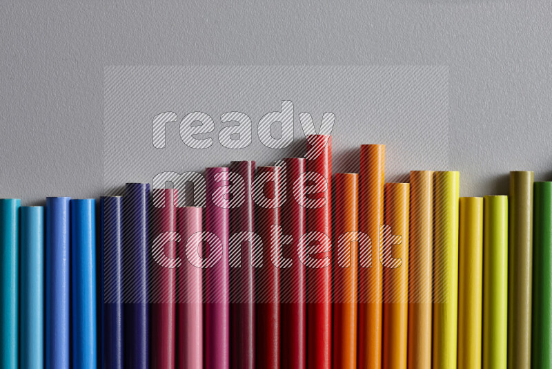 A collection of colored pencils arranged showcasing a gradient of different hues on grey background
