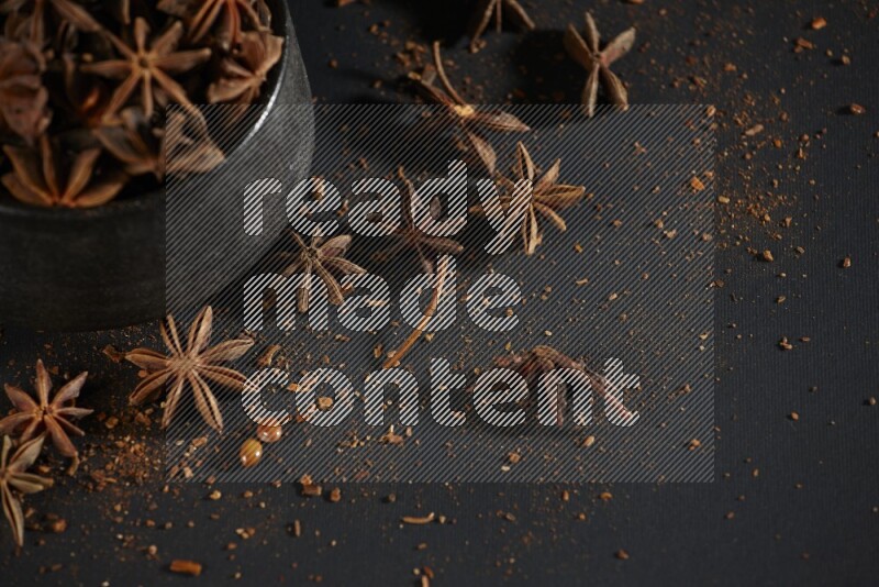 Star Anise in a black bowl with sprinkled anise on black flooring