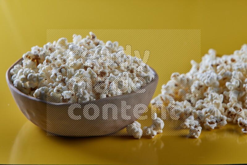 A brown pottery bowl full of popcorn with popcorn beside it on a yellow background in different angles