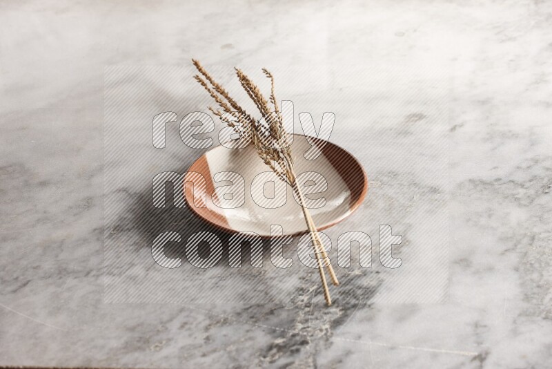 Wheat stalks on multicolored pottery plate on grey marble background