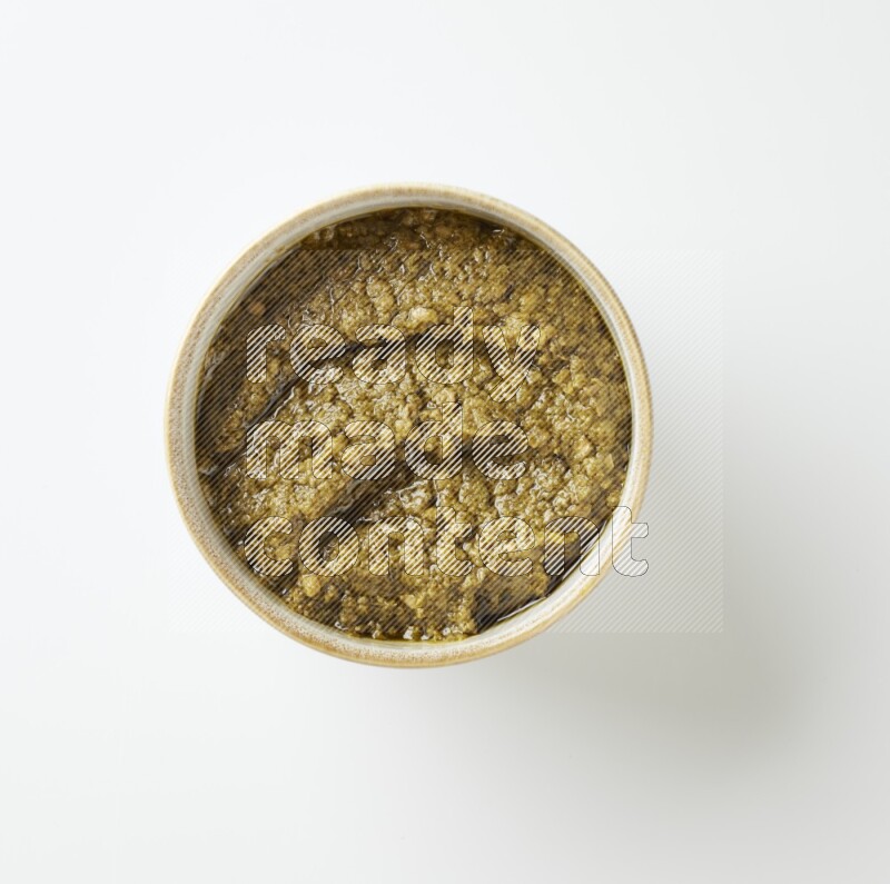 Large multi color pottery round bowl filled with pesto paste on a white counter top