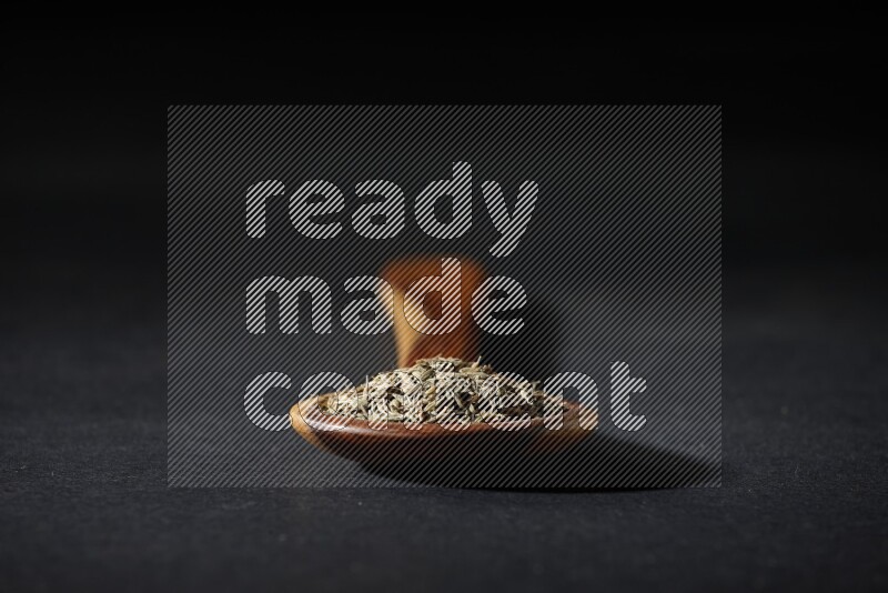 مغرفة خشبية ممتلئة بحبوب الكمون على خلفية سوداء