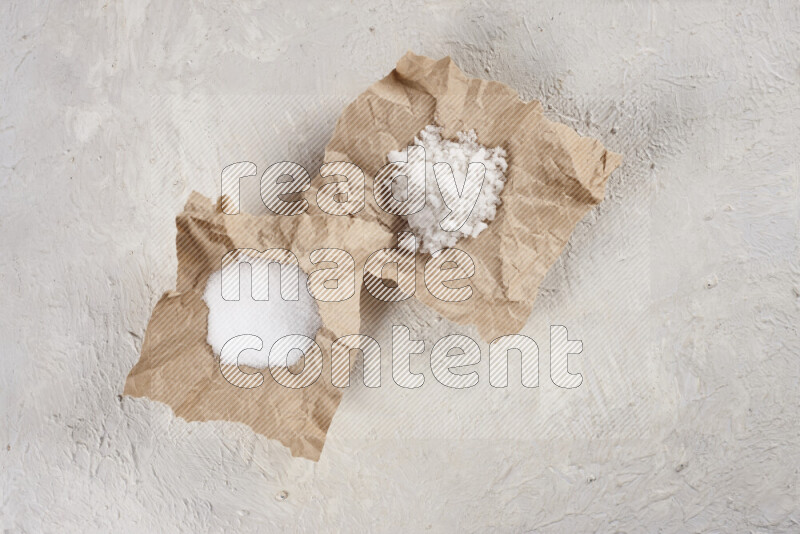 A crumpled piece of paper full of white salt on white background