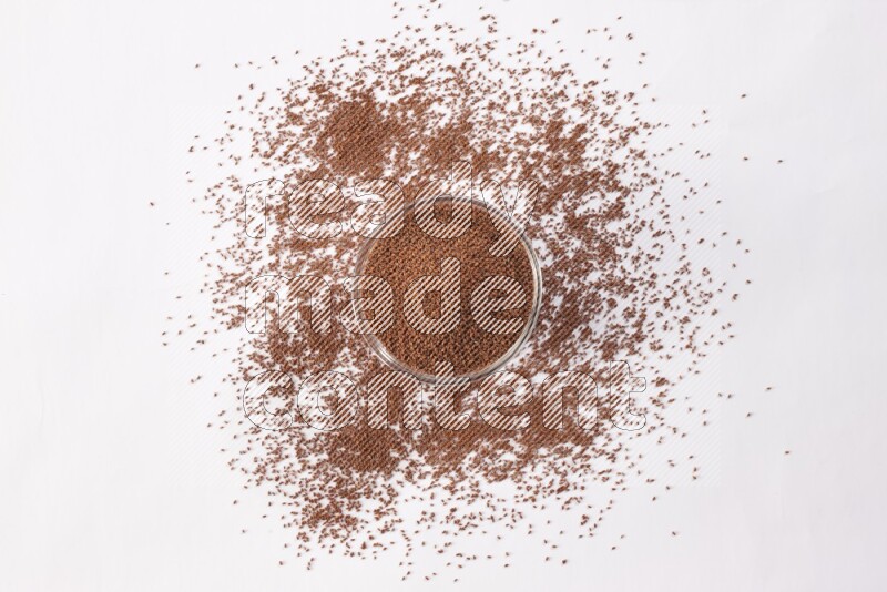 A glass bowl full of garden cress seeds with more seeds spread on a white flooring