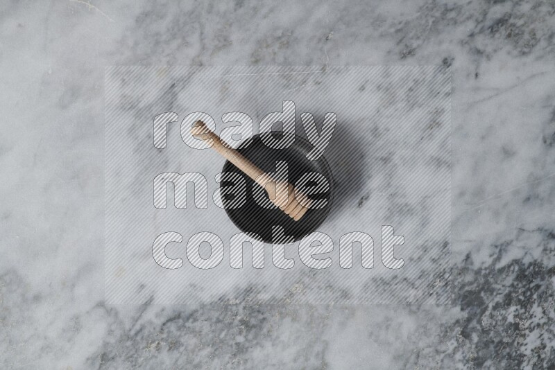 Black pottery bowl with wooden honey dipper in it on grey marble background