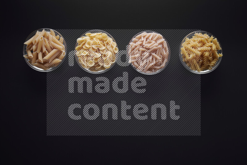 Different pasta types in glass bowls on black background