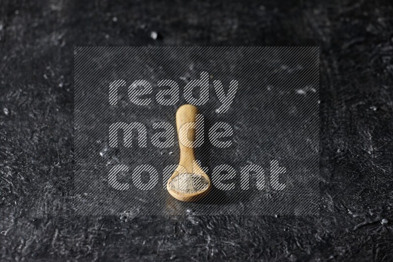 A wooden spoon full of white pepper powder on textured black flooring