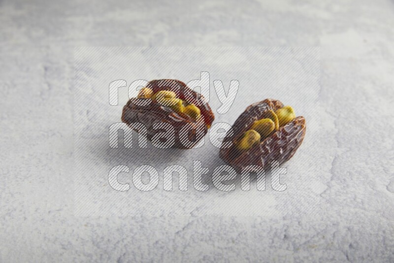 two pistachio stuffed madjoul date on a light grey background