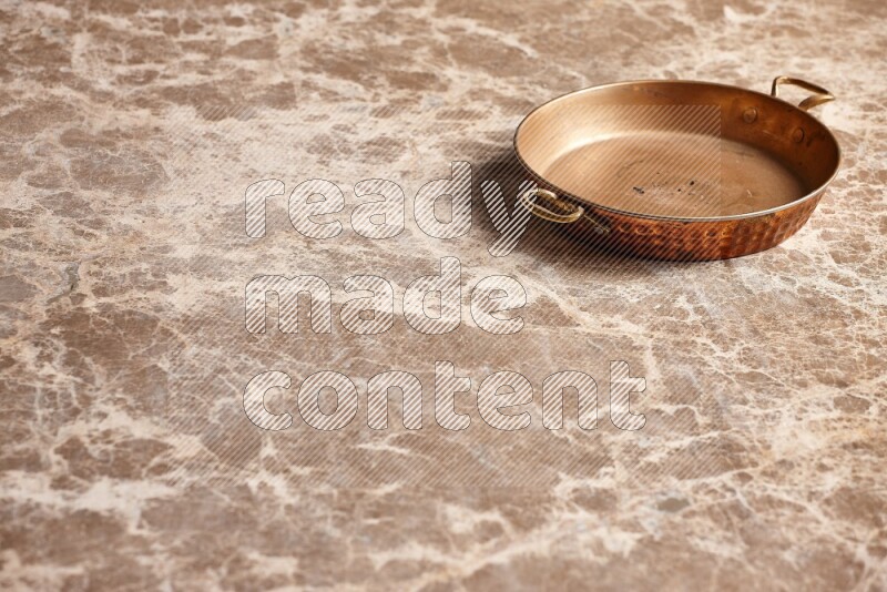 A small copper pan on beige marble background
