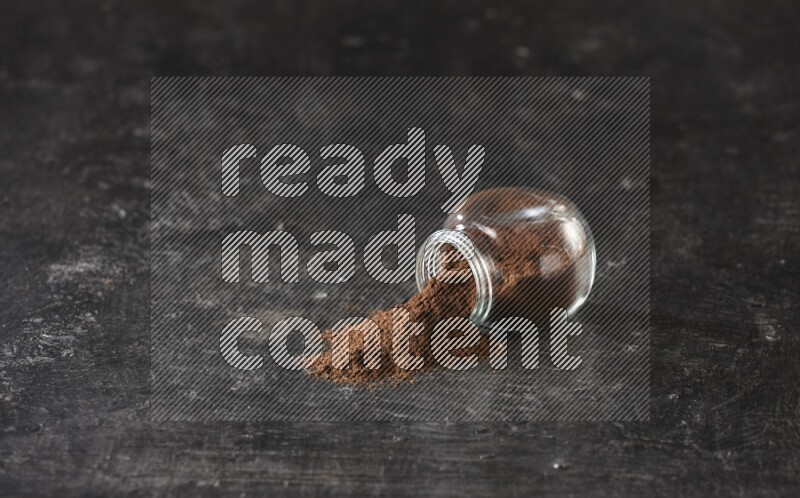 وعاء زجاجي للتوابل مقلوب ممتلئ ببودرة القرنفل والبودرة سقطت منه على أرضية سوداء