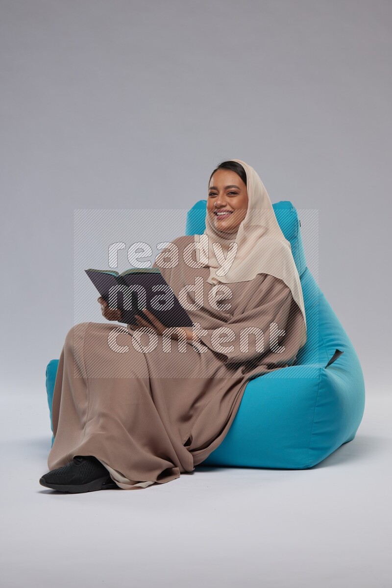 A woman sitting on a blue beanbag and reading a book