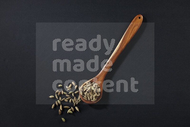 A wooden ladle full of cardamom on black flooring