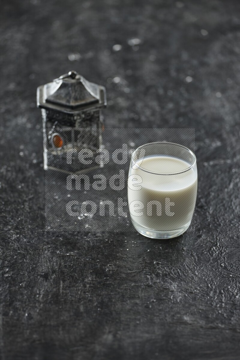 A silver lantern with different drinks, dates, nuts, prayer beads and quran on textured black background