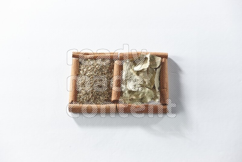 مربعان من أعواد القرفة ممتلئان بأوراق الغار والكمون علي خلفية بيضاء