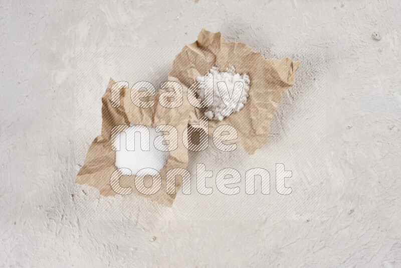 A crumpled piece of paper full of white salt on white background