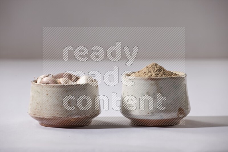 2 beige pottery bowls, one full of garlic powder and the other full of garlic cloves on a white flooring