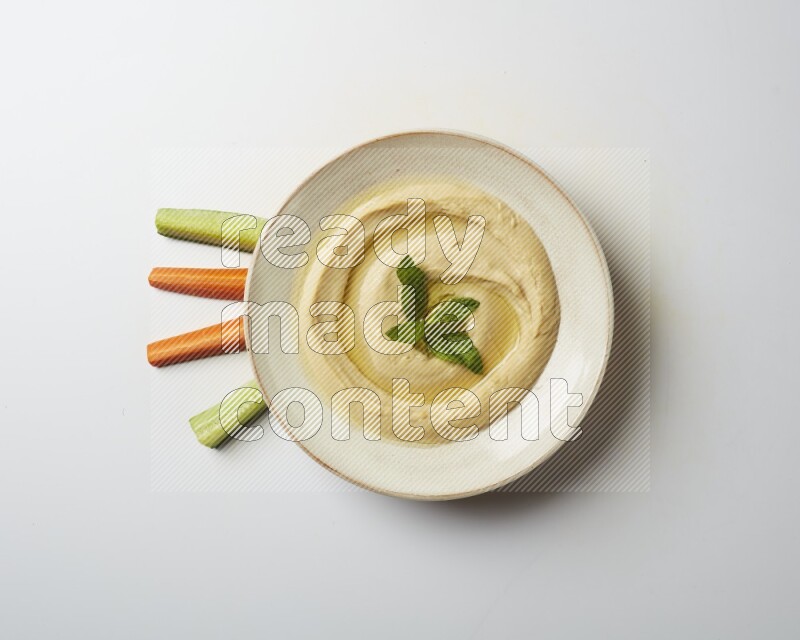 Hummus in a pottry plate garnished with mint  on a white background