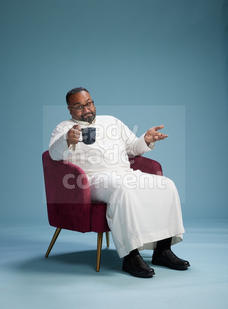 Saudi Man without shimag sitting on chair drinking coffee on blue background