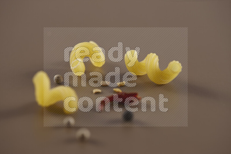 Raw pasta with different ingredients such as cherry tomatoes, garlic, onions, red chilis, black pepper, white pepper, bay laurel leaves, rosemary and cardamom on beige background
